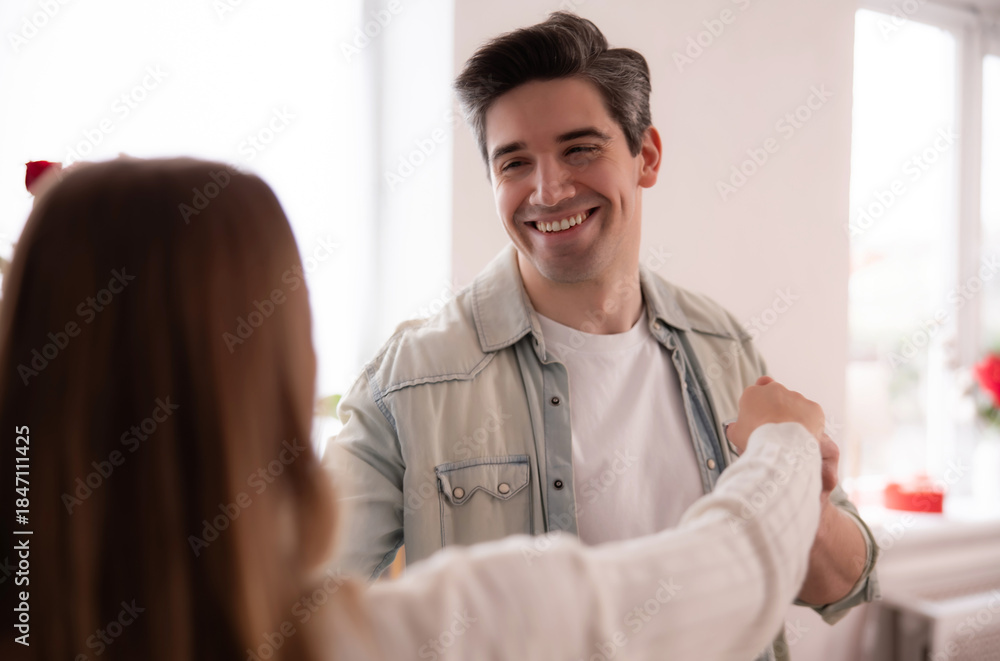 Fototapeta premium Romantic Valentine’s Day love story.Happy young couple dancing at home,holding hands and smiling.Authentic lifestyle moment celebrating love,intimacy,emotional connection in bright modern interior