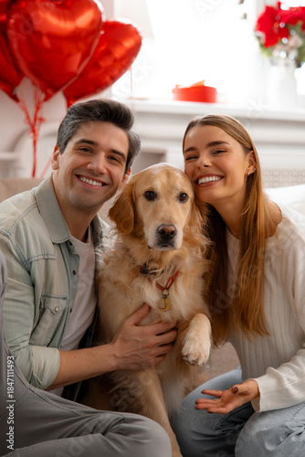 Smiling young couple posing with their dog at home, celebrating Valentine’s Day together. Cozy lifestyle portrait with heart balloons, showing love, family bond, and companionship in a warm interior.