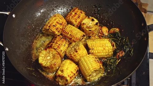 close-up footage of pieces of corn are fried in a pan with garlic and rosemary, barbecue party in evening