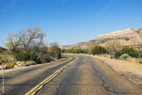 Winding asphalt road through desert landscape. Empty highway leading into rocky hills. Clear blue sky above rural scenery. Travel adventure route in arid nature. Scenic countryside drive