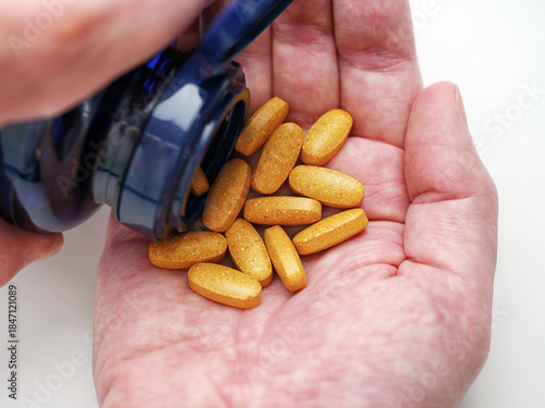 A man taking Vitamin B Complex tablets out of a bottle. Close up.