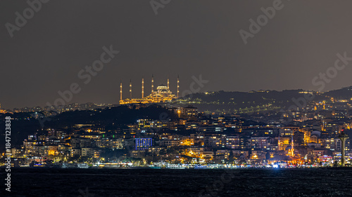 Fotografie Panoramic view of Istanbul skyline with the camlica mosque rising above the city, ferries crossing the bosphorus strait, and dense urban architecture under dramatic clouds