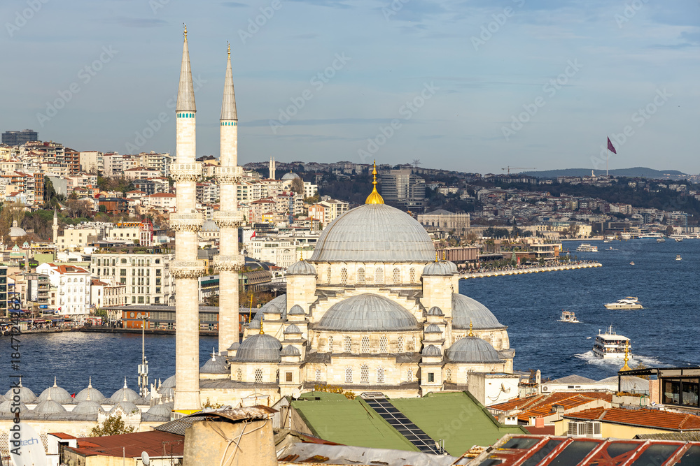 Obraz premium Scenic view of Istanbul along the Bosphorus featuring a monumental Ottoman mosque with twin minarets, dense urban hillside, blue waterway with boats, and bright daylight atmosphere for travel and cult