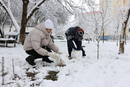 A woman and a boy are playing with snowballs, trying to make a snowman.