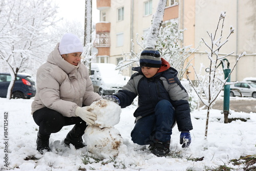 A woman and a boy are playing with snowballs, trying to make a snowman.