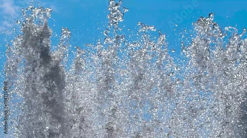 Fountain jet and splashes against blue sky. Spraying clear water into air on summer sunny day in city park. Sparkling water background. 4K footage.