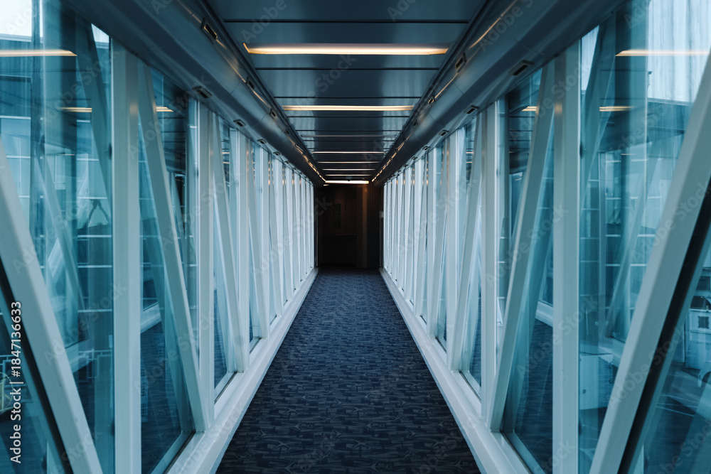 Fototapeta premium Airport jet bridge corridor interior. Long glass walkway perspective. Empty passenger boarding tunnel. Modern terminal architecture design. Symmetry lines and vanishing point. Travel concept.