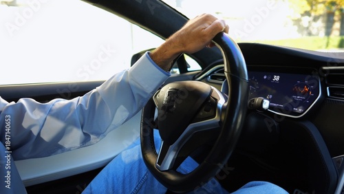 Obraz na plátne Male hand of businessman holds steering wheel while driving electrical vehicle at city