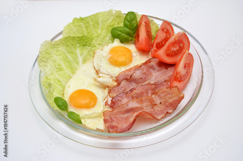 A hearty breakfast on a plate of scrambled eggs with bacon, tomatoes and herbs