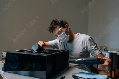 Focused computer repair professional wearing protective mask and safety glasses cleaning computer interior with vacuum, preventing dust accumulation and potential hardware damage.