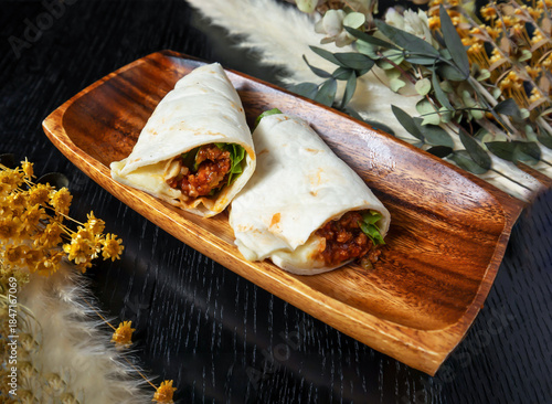 Delicious burritos on wooden plate with fresh flowers