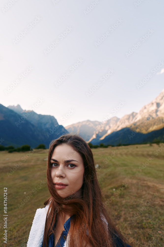 Naklejka premium Woman portrait in mountains meadow nature landscape outdoors traveler looking at camera with long hair and soft light, scenic valley background for travel, adventure and calm mood.