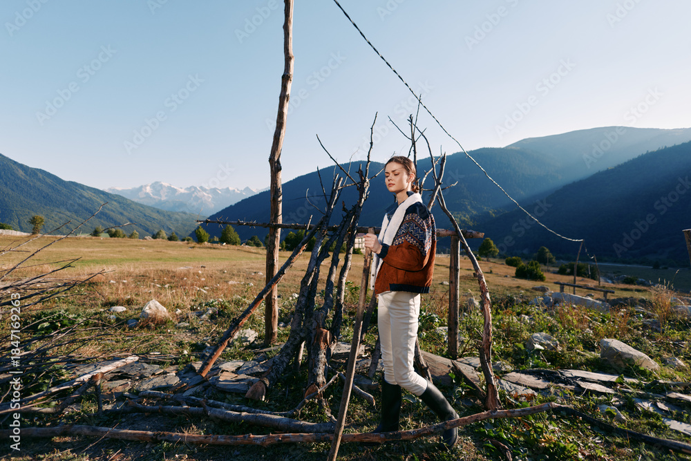 Naklejka premium woman mountains field cup sweater rural nature standing by a rustic stick fence in an alpine valley, cozy jacket and boots enjoying morning sunlight and scenic mountain landscape