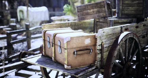 A weathered wooden cart displays two vintage suitcases in a rural area. Surrounding elements hint at a bygone era, creating a nostalgic atmosphere filled with history and charm.