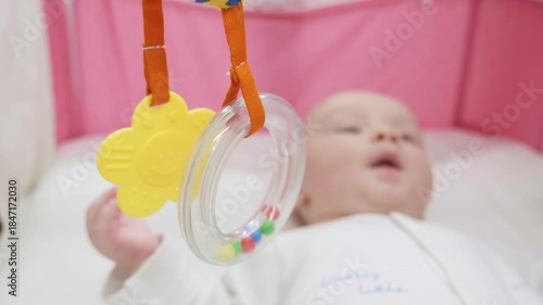 Newborn is awake in crib with hanging toys over him. 1 month old baby looking at hanging baby mobile with selective focus. Handheld high angle shoot with shallow depth of field