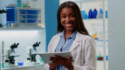 Smiling african american scientist in a modern lab studies data and records findings on a digital tablet while surrounded by lab equipment, flasks and microscope