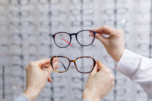 Fototapeta Hands comparing two eyeglass frames in optical store choosing eyewear for vision