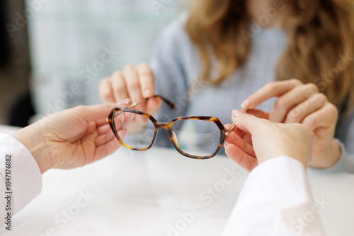 Optician showing eyeglass frame to customer at counter during prescription eyewear fitting