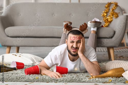Young man in reindeer horns with hangover lying after Christmas party at home