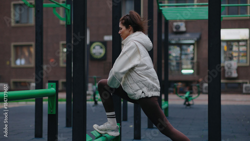 Fotografi Young woman stretches at a fitness park in the afternoon sun while preparing for