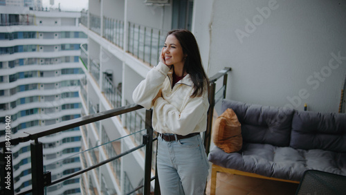 Young woman stands on balcony overlooking city, enjoying a moment of relaxation and fresh air during daytime at a modern apartment