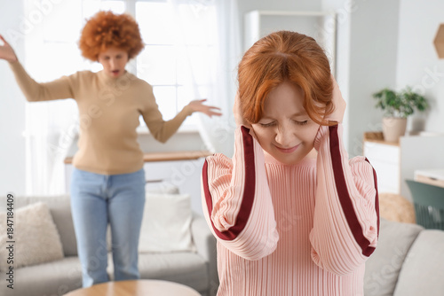 Redhead teenage girl covering her ears during squabble with mother at home