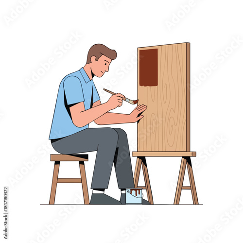 A man paints on a wooden canvas, using a brush, seated on a stool, next to an easel