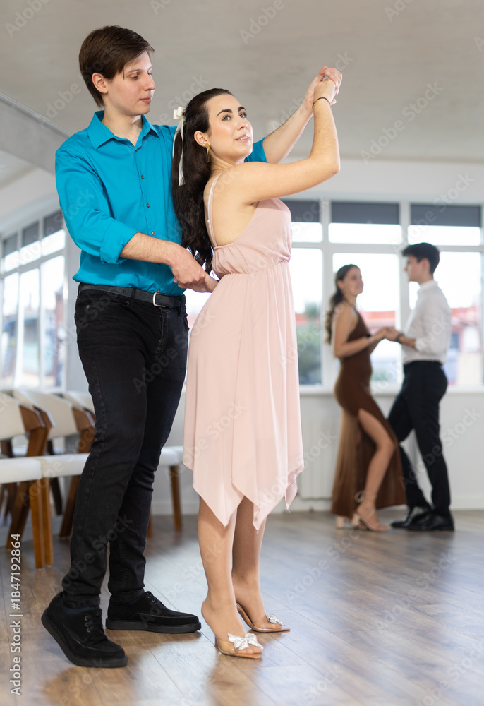 Naklejka premium Happy girl and guy enjoying passionate latin american dancing with male partner in dance hall