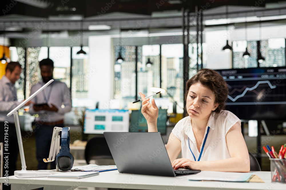 Obraz premium Pensive businesswoman playing with pen and contemplating over resource allocation in multinational company. Female manager focuses on laptop, evaluating budget funds and planning financial strategies.