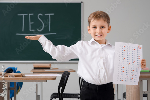 Cute schoolboy with results of test in classroom