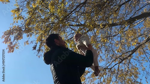 Loving father playing with baby son under tree