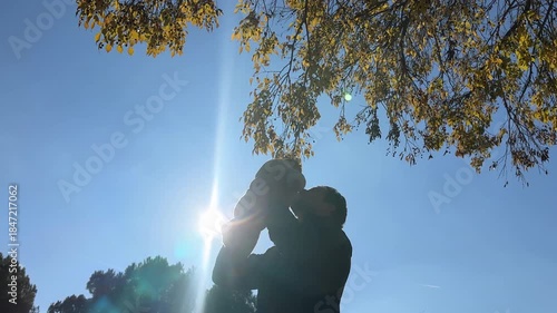 Happy father lifting his baby up high in a park with sun flare