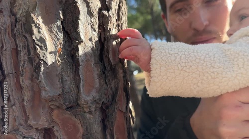 Father introducing his baby to nature touching a tree trunk