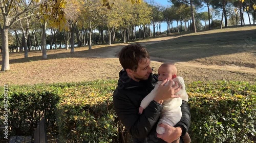 A father holds his child in his arms while they smile on a sunny day in the park