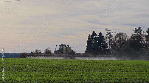 A tractor cultivates the fields. The tractor sprays green shoots in the field.A tractor-mounted irrigation system in operation. Agricultural work .Autumn sowing and processing of winter crops. 