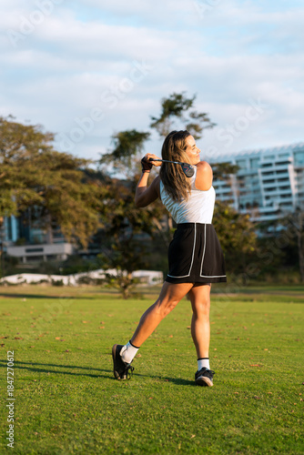 Latin hispanic woman playing golf, swinging club on a sunny green golf course, enjoying leisure and sport outdoor activities