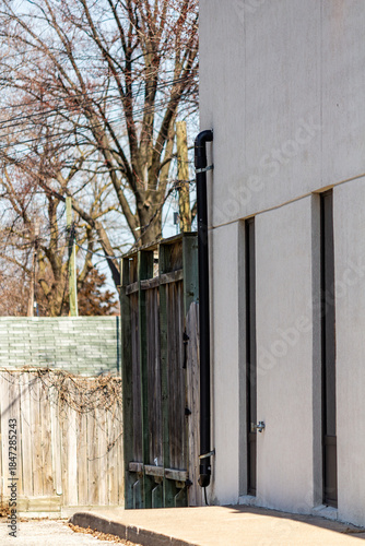Side View Of Building Exterior With Drain Pipe, Wooden Fence, And Winter Trees
