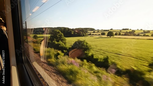 View from a train window of green fields and trees under a clear sky, blurred at lower edge due to motion