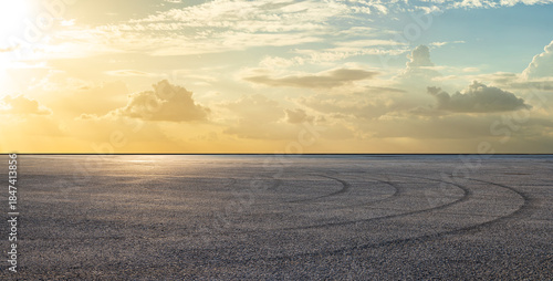 Empty asphalt race track road with tire tracks and beautiful sky clouds at sunset