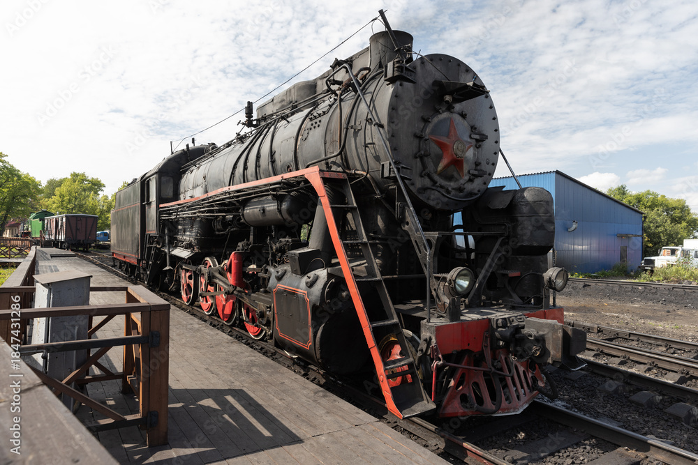 Fototapeta premium A vintage steam locomotive sits on a rail yard track beside a wooden platform