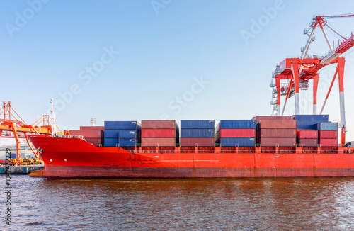 Industrial container ship with containers and gantry cranes at Sea  Port. Large red container vessel docked at Osaka Bay port, Japan. Features heavy-duty gantry cranes and stacked shipping containers.