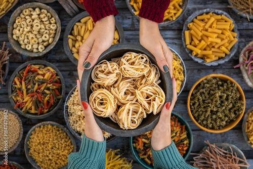 Different types of uncooked pasta at the hands of two women.