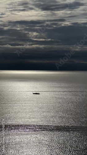 Serene lone boat drifting across shimmering sea under dramatic cloudy sky