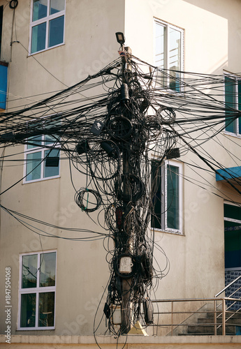 Urban utility pole with tangled wires in a city setting near buildings