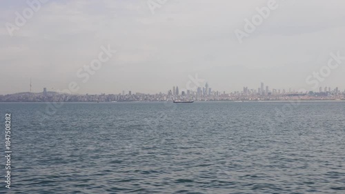 Panoramic view of Istanbul's modern skyline across the water, featuring prominent skyscrapers and a ship on the Bosphorus.