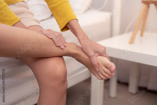 Woman holding her heel and arch in pain, indicating plantar fasciitis, foot fatigue, or heel inflammation from prolonged standing or walking. Indoor recovery scene.