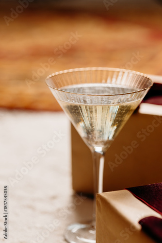 Champagne coupe glass on neutral background with gift box. Minimal festive still life and elegant holiday drink concept.