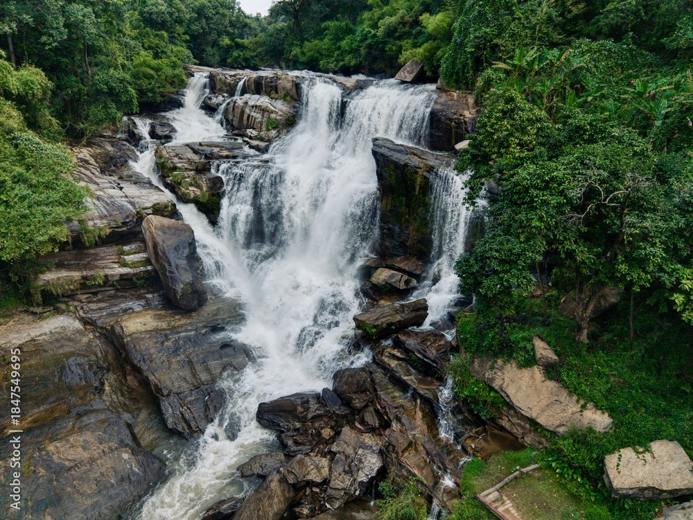 Naklejka premium Close aerial of powerful waterfall over rocks in lush forest