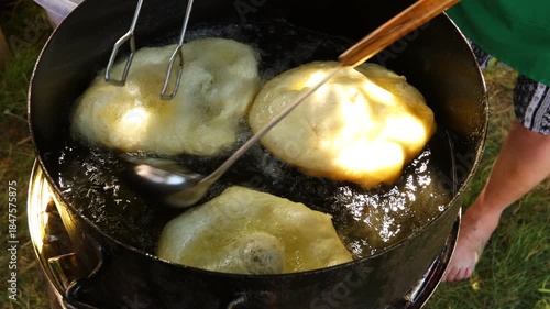 Traditionally way of cooking, frying dough in oil or pork fats making delicious treat in a large rustic pot, deep iron cauldron over open fire.
