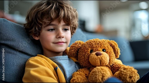 Happy Young Boy with Curly Hair Cuddles His Favorite Teddy Bear on a Cozy Sofa.